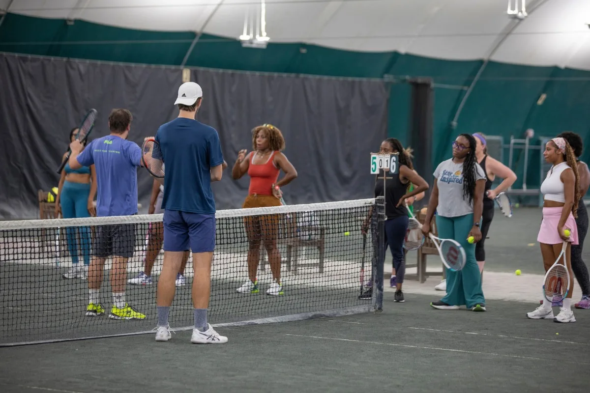 Coach instructing adult students at the net on an indoor court at USTA Midwest Tennis Center in Indianapolis
